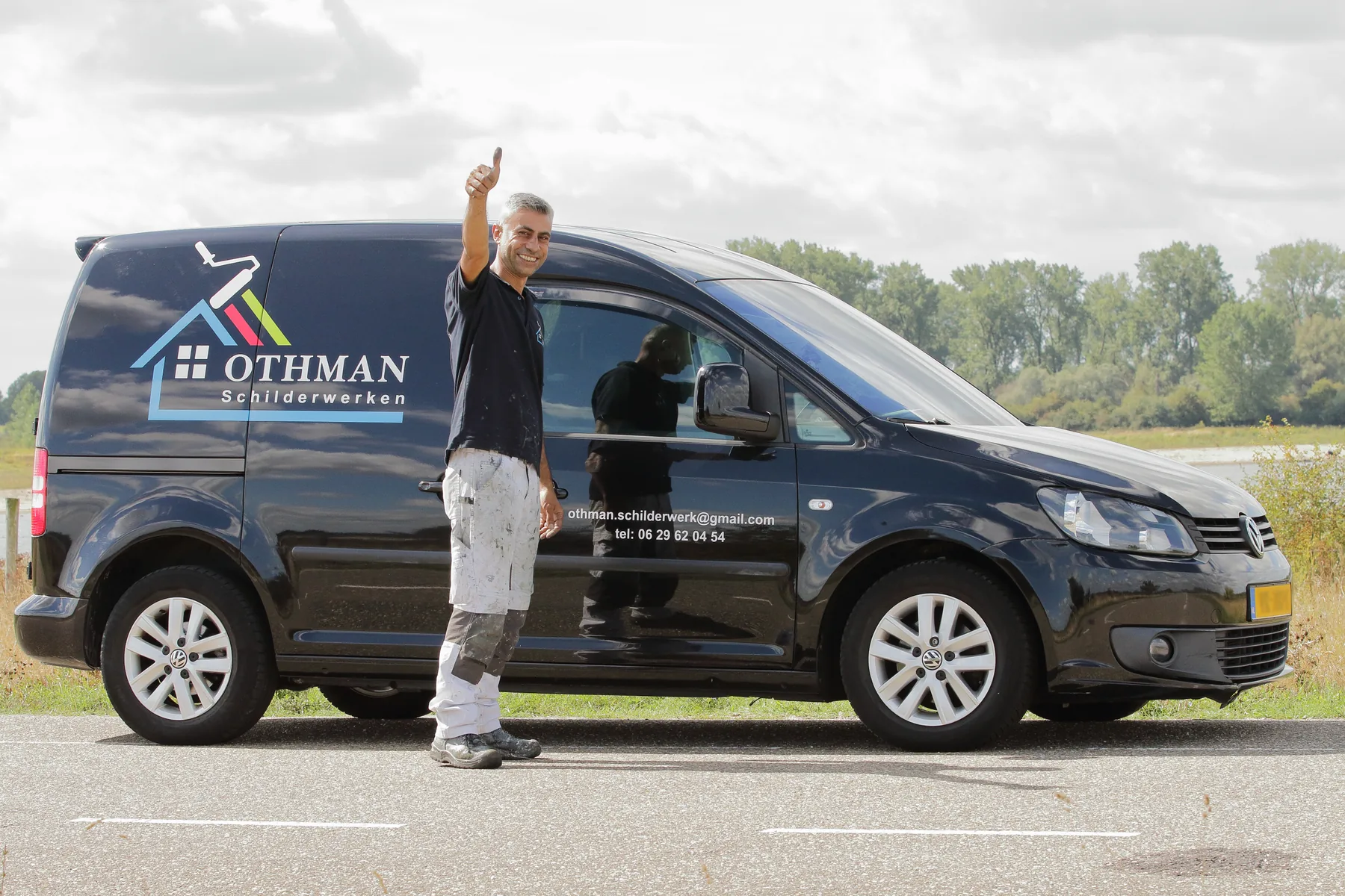 Ali van Othman Schilderwerken staat naast zijn bedrijfsbus en steekt zijn duim op