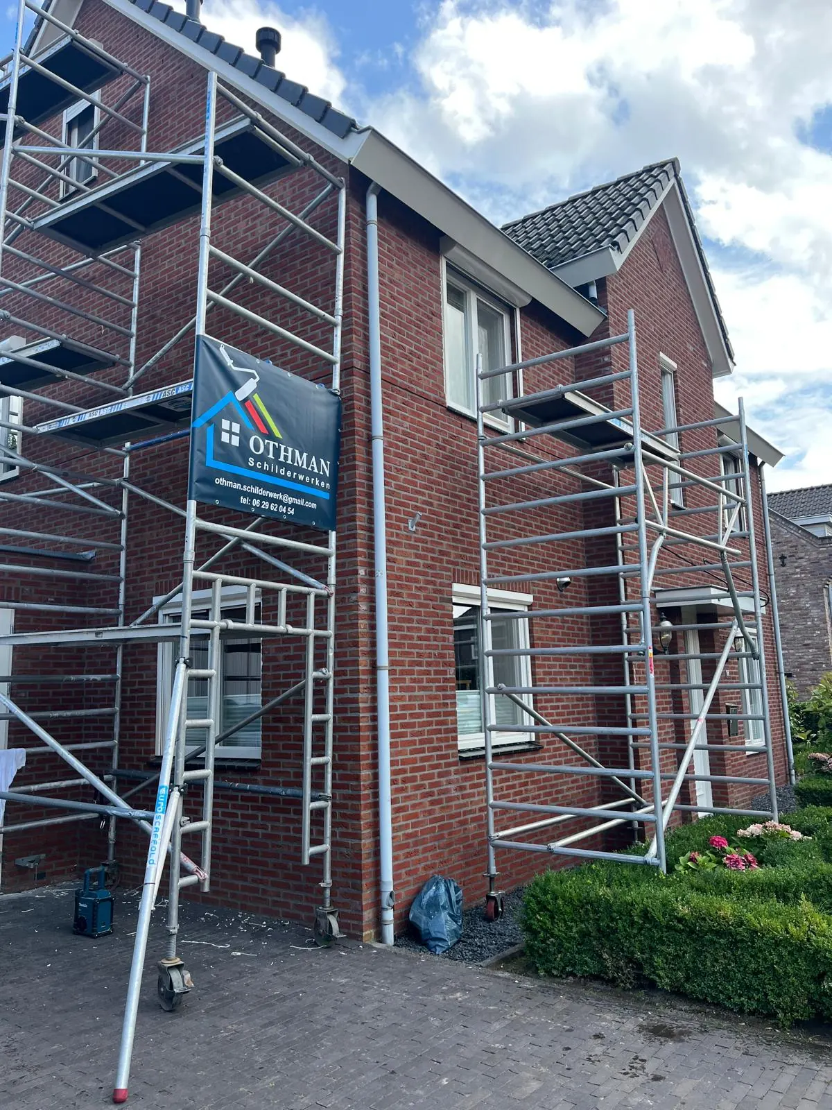 Een woning met steigers en een spandoek van Othman Schilderwerken tijdens buitenschilderwerk.