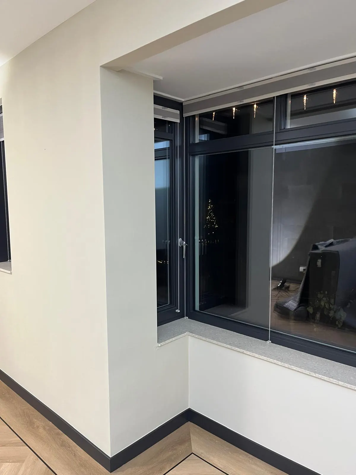 Een strak afgewerkte lichte binnenwand naast donkere raamkozijnen.