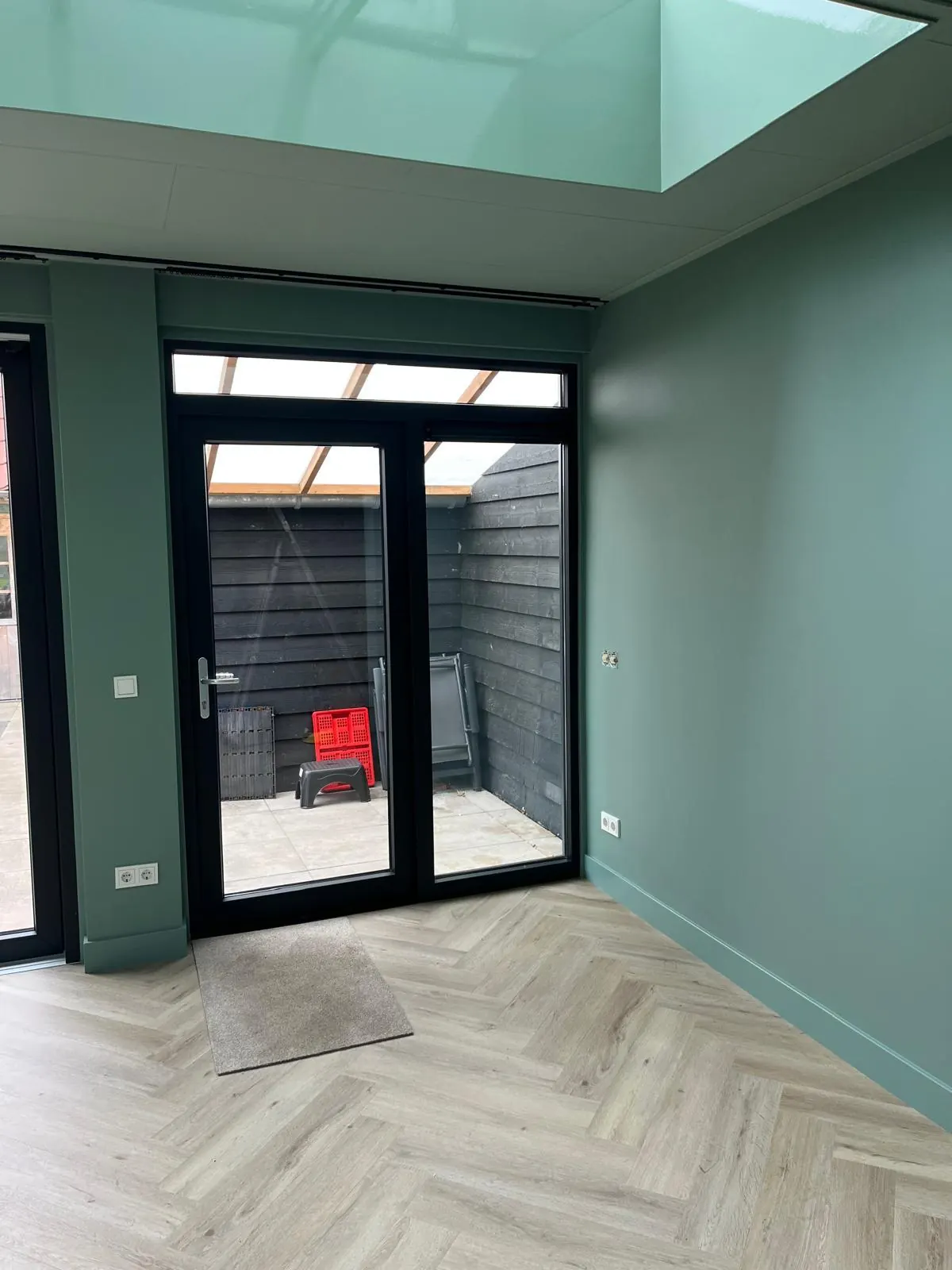 Een lichte uitbouw met groen geschilderde wanden en bijpassende plinten.