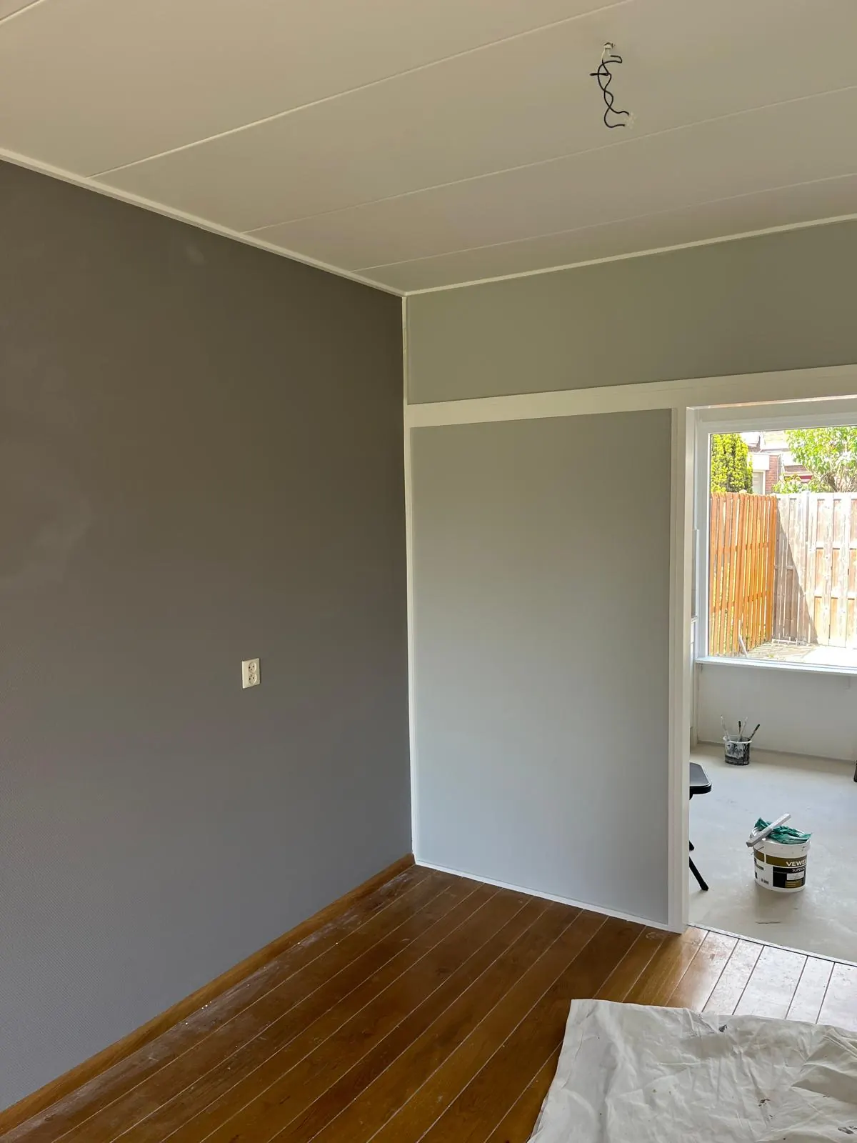 Een kamer in uitvoering met grijs geschilderde wanden, een wit plafond en witte lijsten.